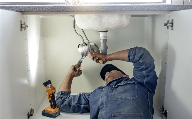 Plumber repairing pipes beneath a bathroom sink in Watsonville