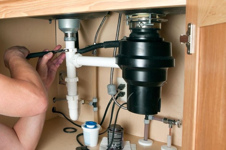 Plumber installing a garbage disposal beneath a kitchen sink in Watsonville