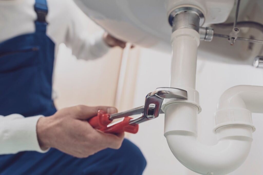 Plumber repairing a white drain pipe beneath a sink in Watsonville
