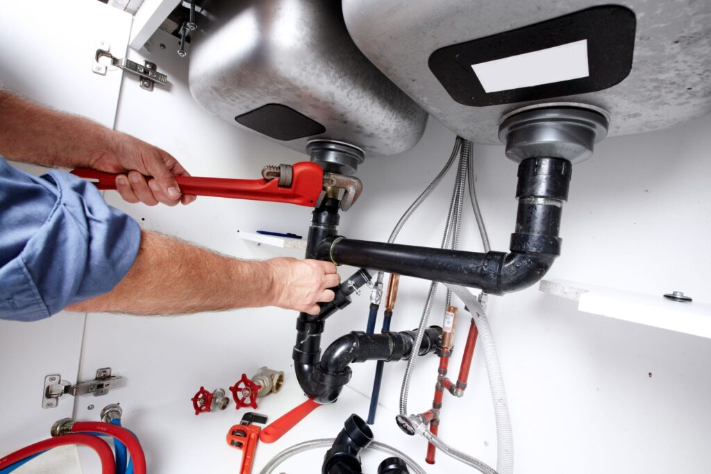 Plumber repairing drain pipes beneath a kitchen sink in Watsonville